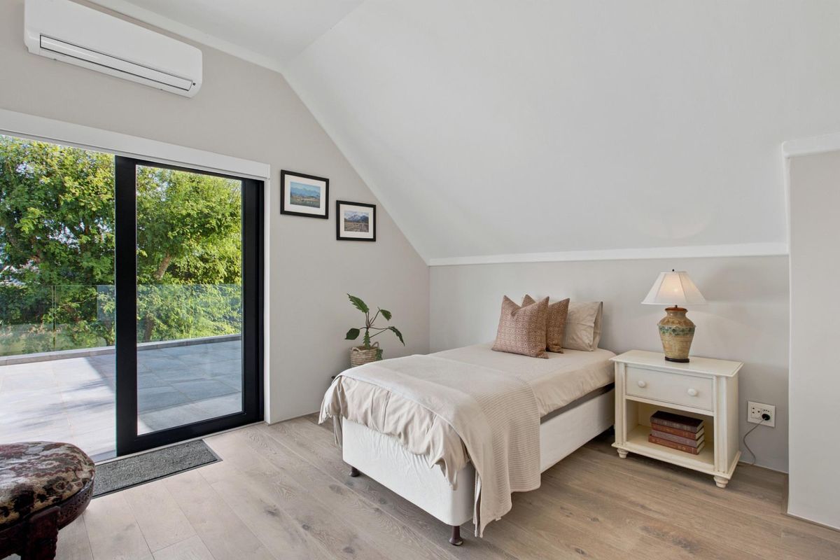 A bright, modern bedroom featuring timber flooring, a split-system air conditioner, and a sliding glass door leading to an outdoor balcony.