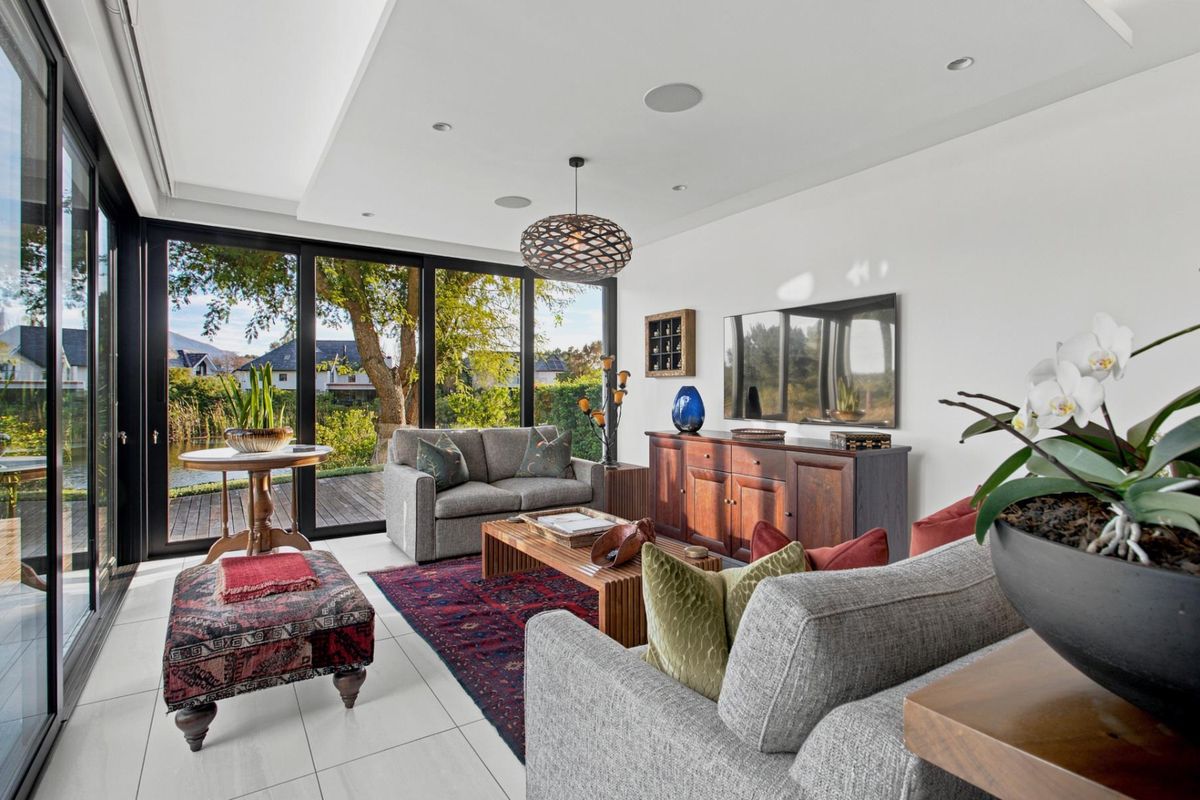 Modern living room featuring large format floor tiles, recessed ceiling lighting, integrated speakers, and expansive black aluminium sliding doors opening to a garden view.
