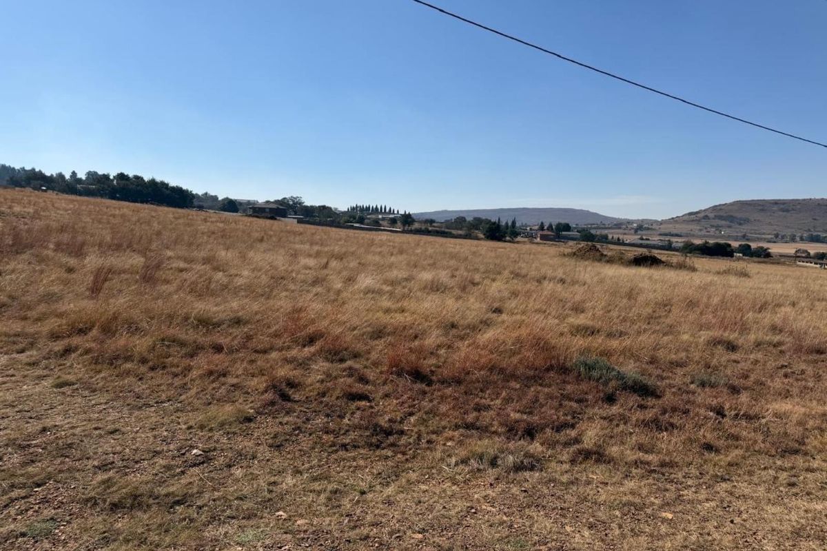 A wide-angle view of a vacant residential plot featuring natural grass terrain and distant landscape views.