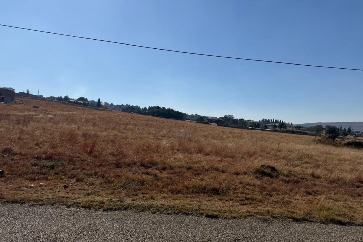 A view of a vacant residential plot of land featuring open grassland and a gentle slope.