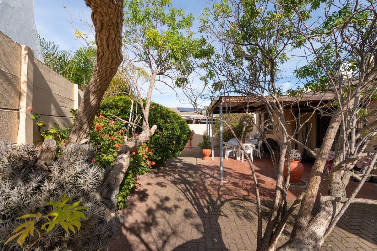 A rear garden area featuring a paved patio with a covered pergola structure and established garden beds enclosed by a boundary wall.