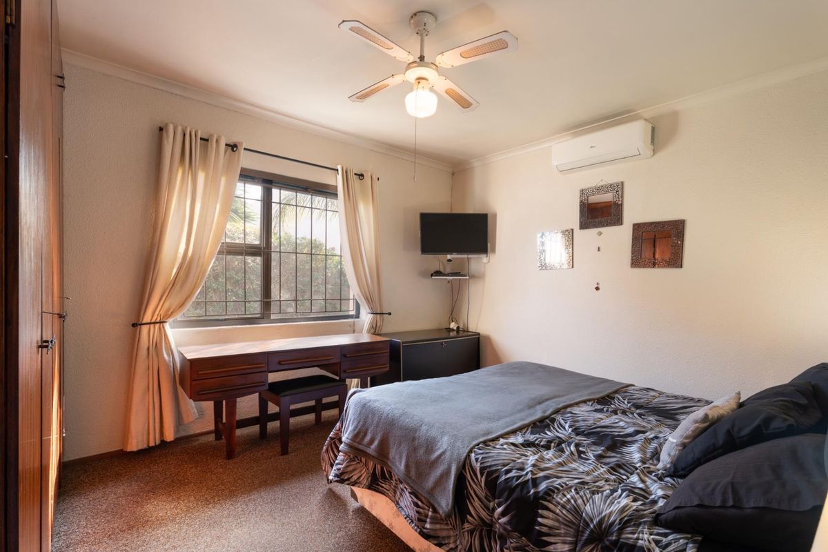 A functional bedroom featuring a ceiling fan, split-system air conditioning, and built-in wardrobe storage, with security bars installed on the window.