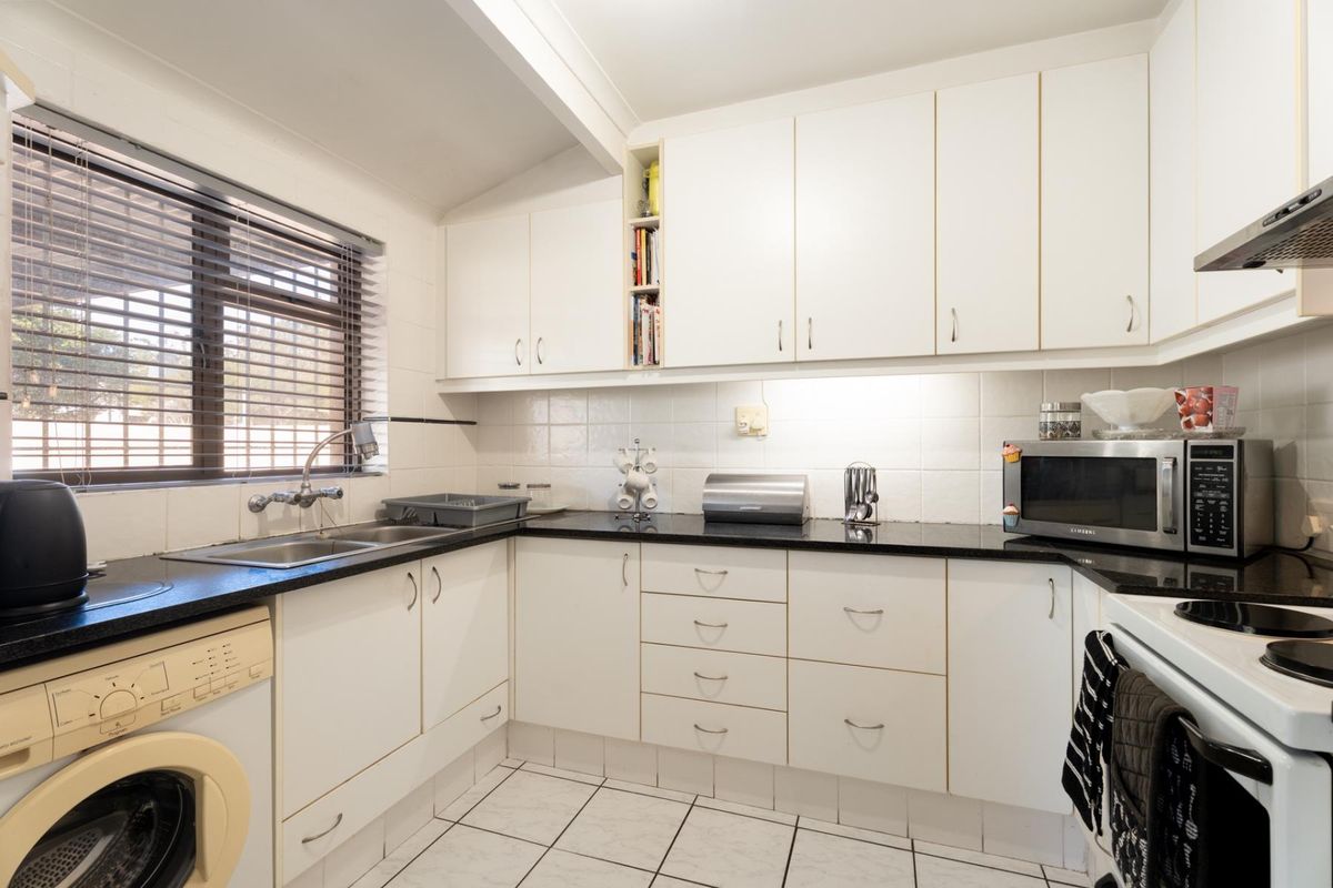 A functional kitchen featuring white cabinetry, dark granite countertops, tiled backsplash, and integrated laundry plumbing, offering a clean and practical workspace.