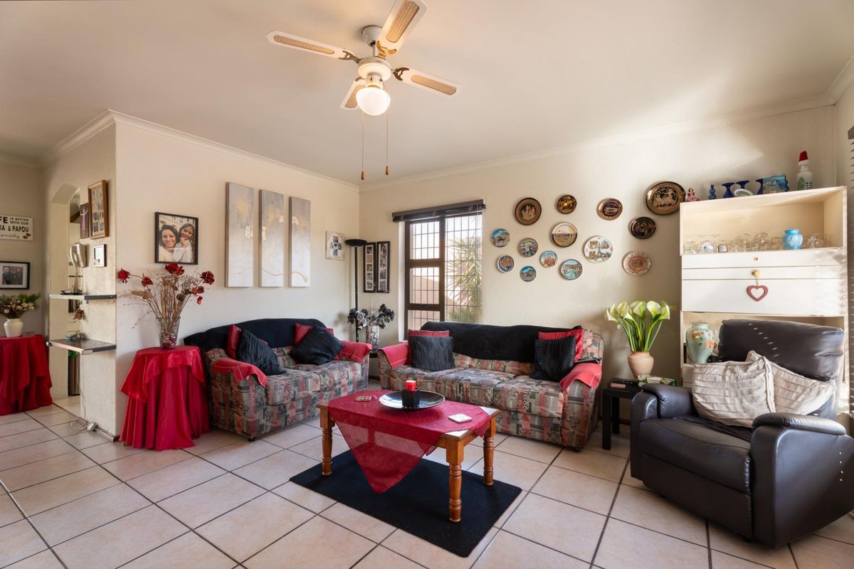 A living room featuring tiled flooring, a ceiling fan, and security bars on the window, offering a functional space with neutral wall finishes.