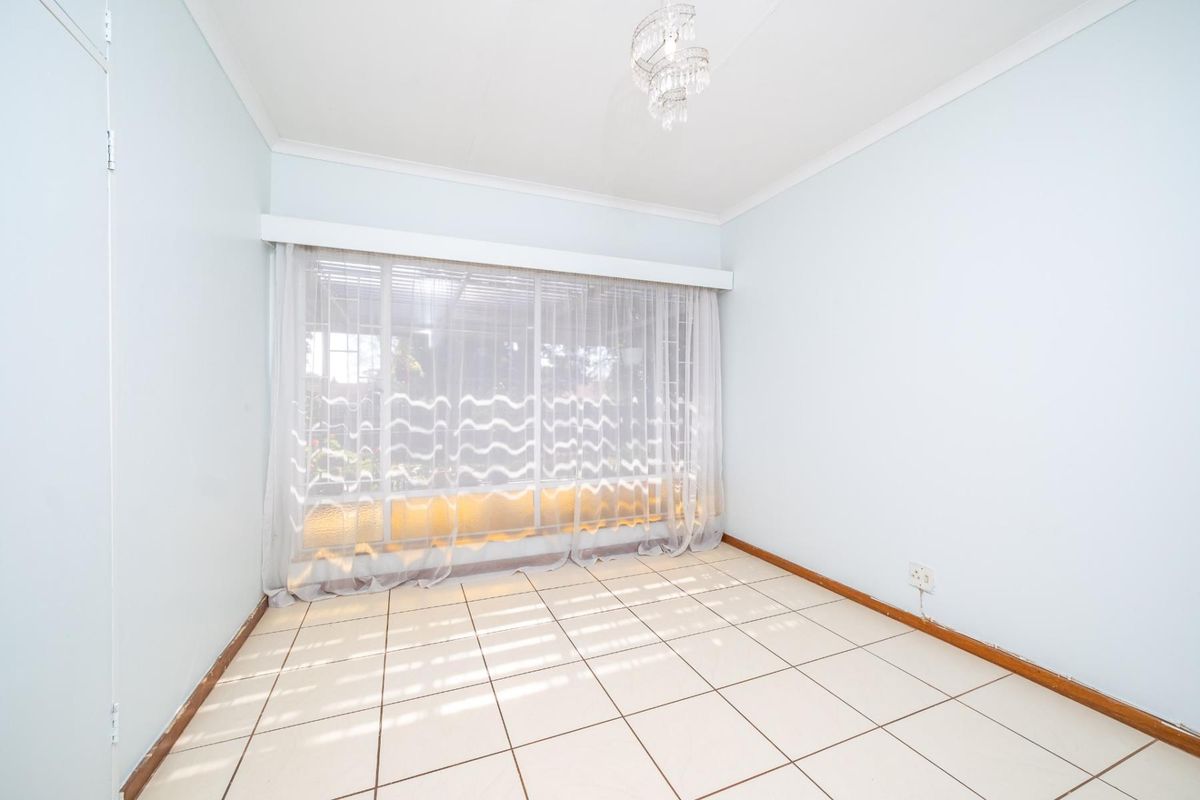 A bright, empty bedroom featuring tiled flooring, a large window with natural light, and built-in storage space.
