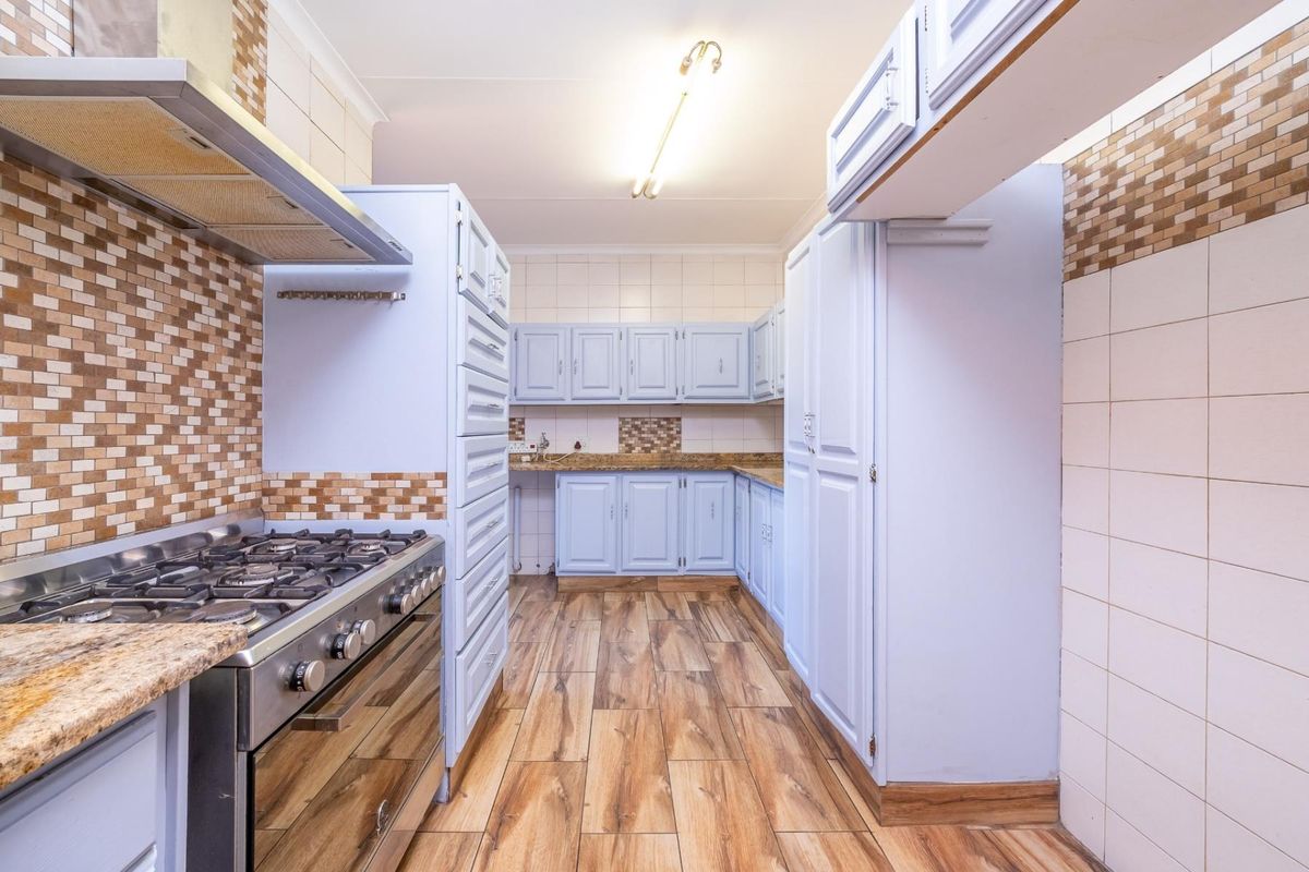 A functional kitchen featuring light blue cabinetry, granite countertops, a gas stove with extractor fan, and wood-look tiled flooring.