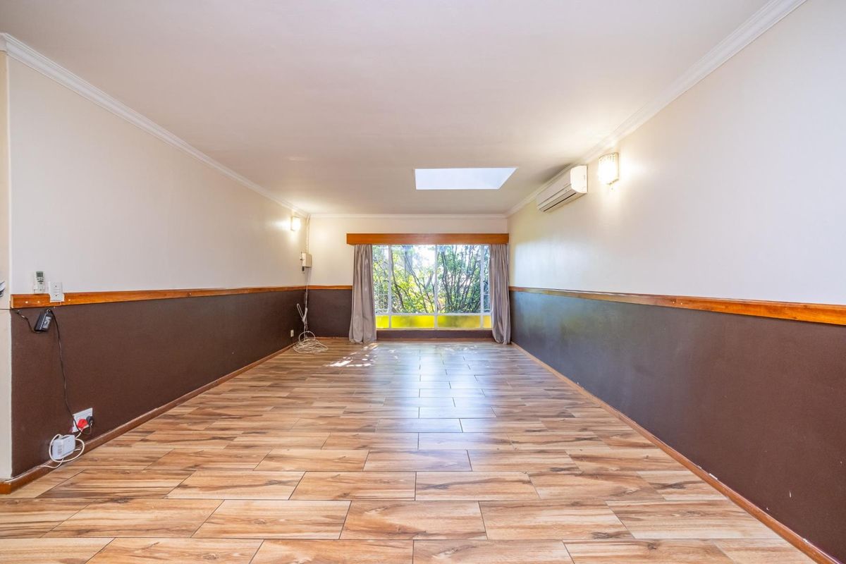 A spacious, empty living room featuring wood-look tile flooring, wainscoting, a skylight, and a wall-mounted air conditioning unit.
