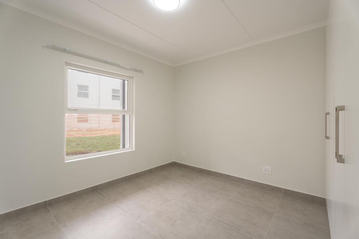 A clean, empty bedroom featuring neutral tiled flooring, built-in cupboards, and a window providing natural light.
