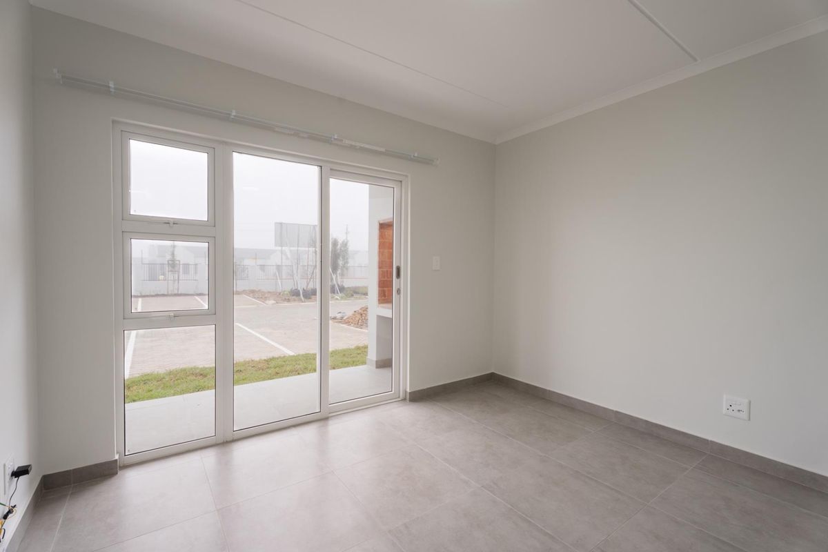 A bright, empty living area featuring neutral tiled flooring and a large sliding glass door providing access to the exterior patio.