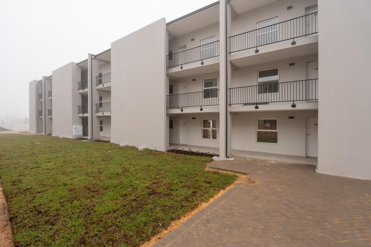 Exterior view of a modern apartment complex featuring multi-level balconies with metal railings, paved walkways, and a newly established lawn area.