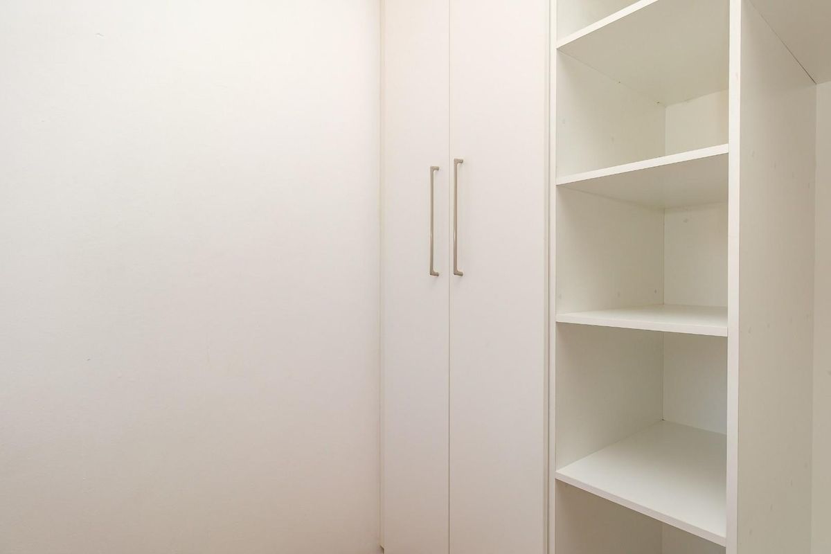 A clean and minimalist bedroom space featuring white built-in cupboards and integrated shelving for efficient storage.
