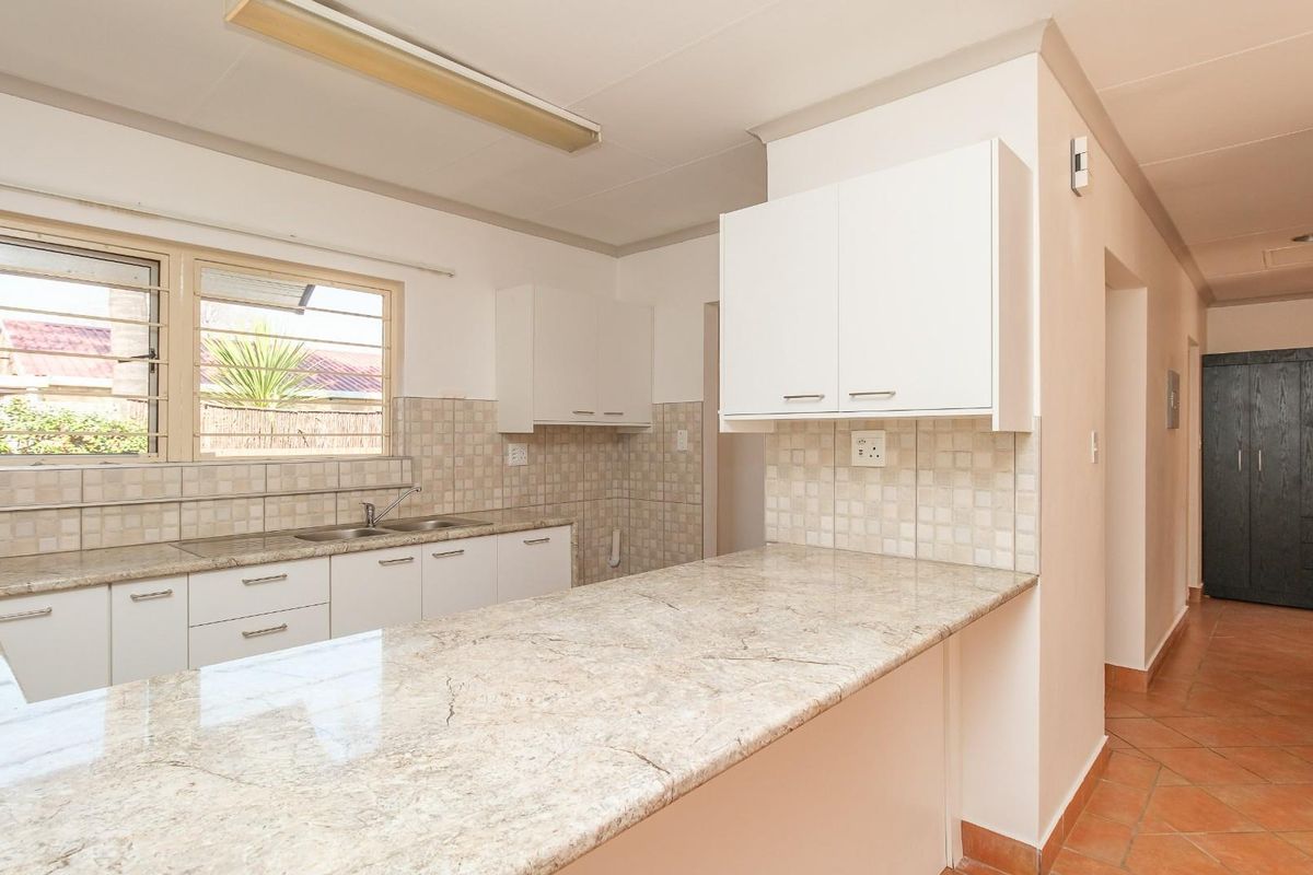 A functional kitchen featuring granite countertops, ample built-in cabinetry, a double basin sink, and tiled backsplash, leading into a tiled hallway.