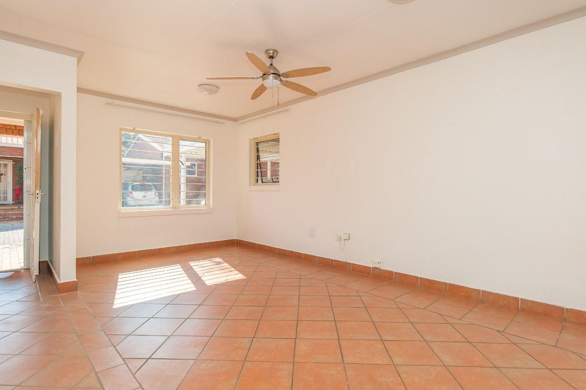 A bright, empty living room featuring terracotta floor tiles, a ceiling fan, and natural light from aluminium-framed windows.