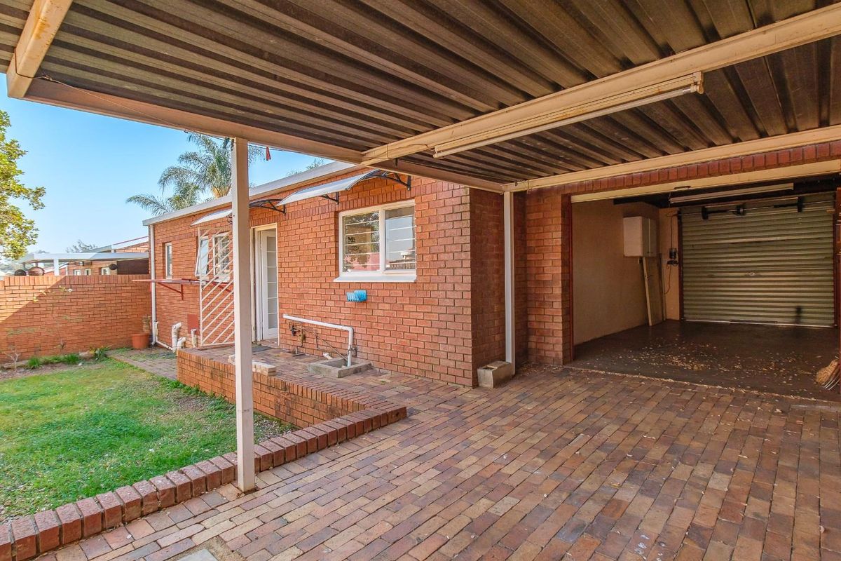 Rear exterior view featuring a paved patio area, brick facade, and an attached garage with a roller door.
