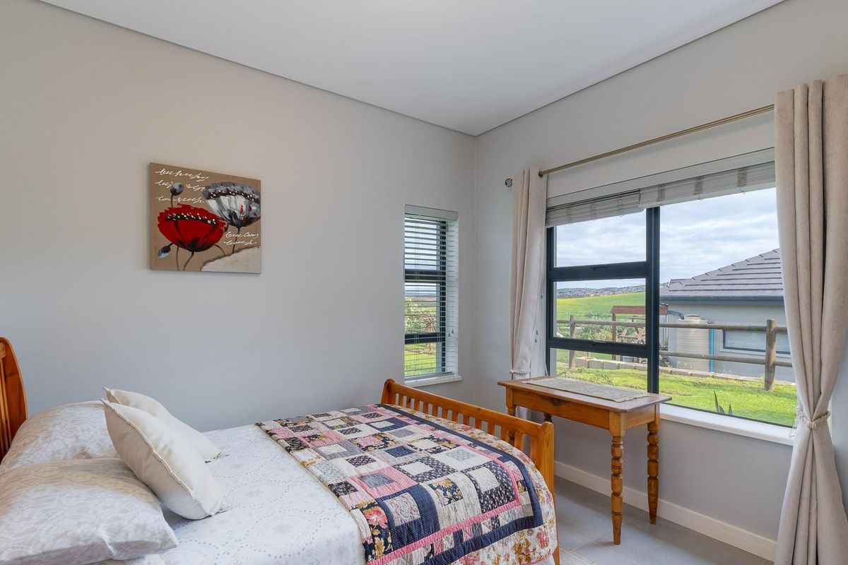 A bright and well-maintained bedroom featuring neutral walls, aluminium window frames, and views over the surrounding landscape.