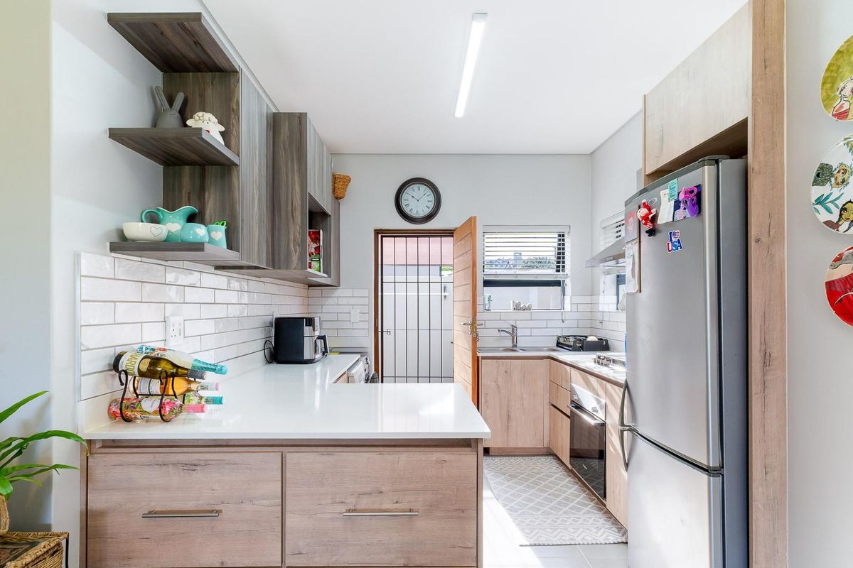 Modern kitchen featuring light wood cabinetry, white quartz countertops, subway tile backsplash, and integrated stainless steel appliances with direct access to the exterior.