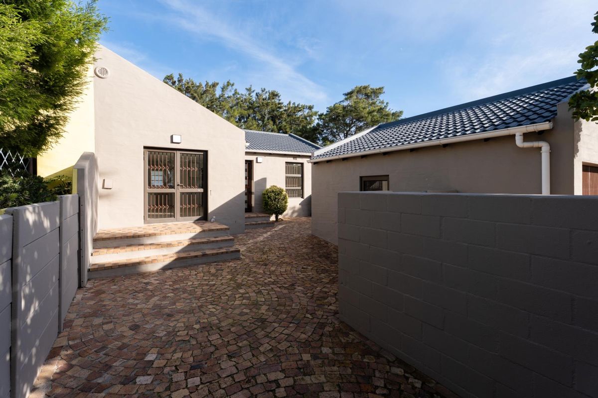 A well-maintained rear courtyard featuring cobblestone paving, secure access points, and clean exterior finishes under a clear blue sky.