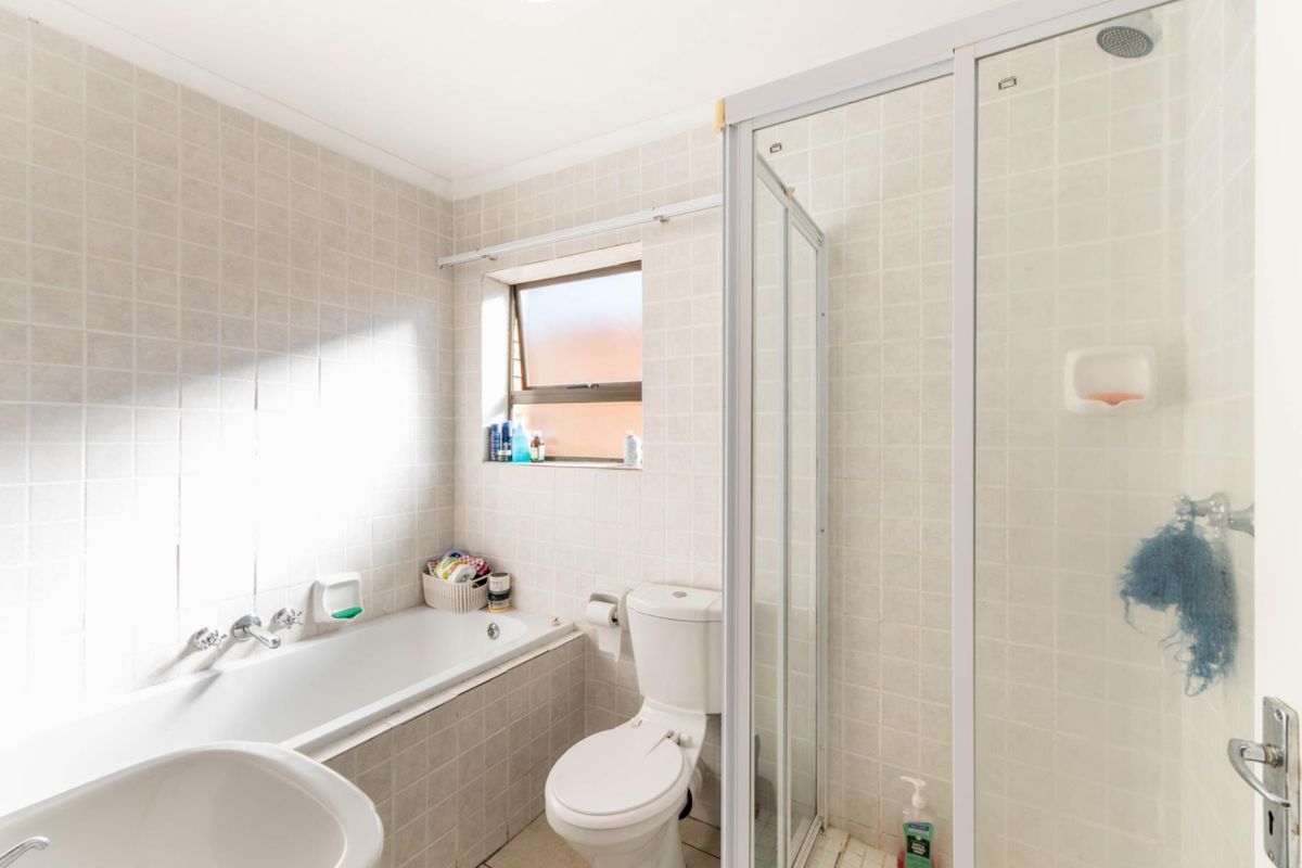 A functional bathroom featuring a built-in bathtub, separate shower enclosure, and tiled finishes throughout, offering a clean and practical layout.
