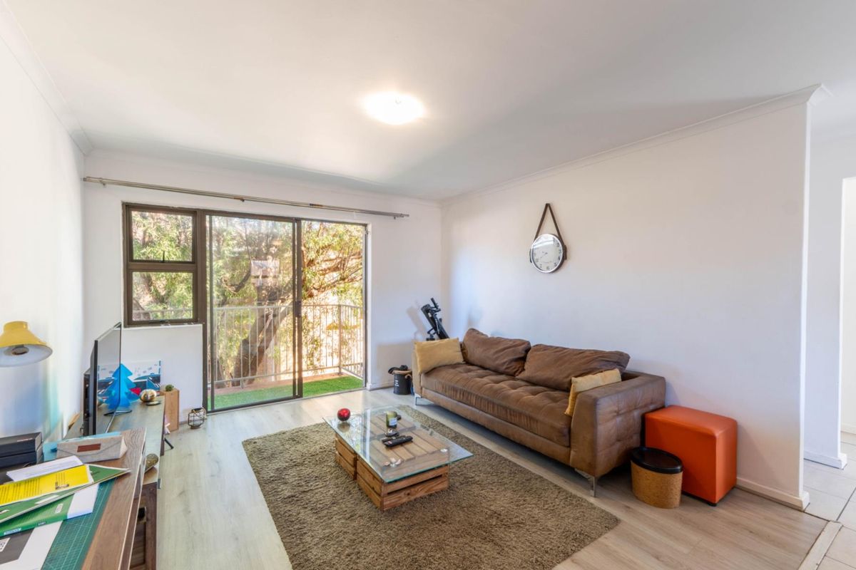 A bright living room featuring laminate flooring and a large sliding glass door that provides access to an outdoor balcony area.