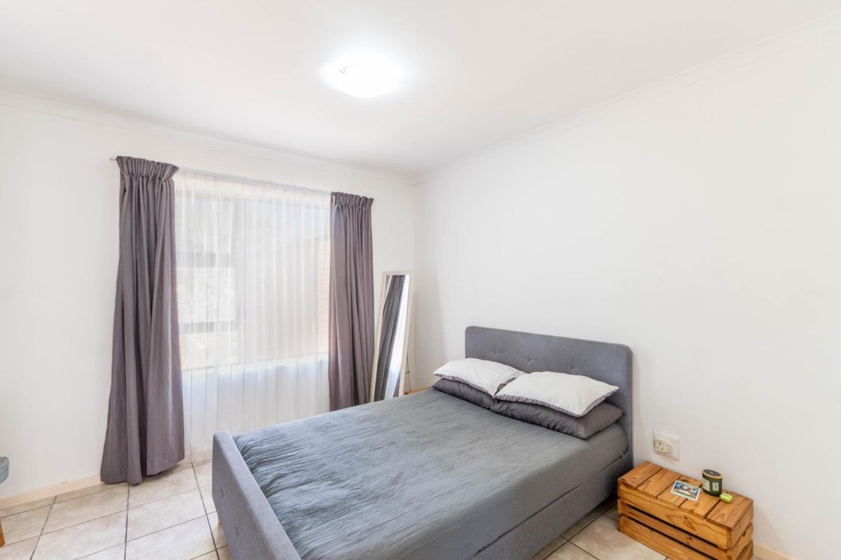 A bright and neutral bedroom featuring tiled flooring and large windows with curtains, providing a clean and functional living space.