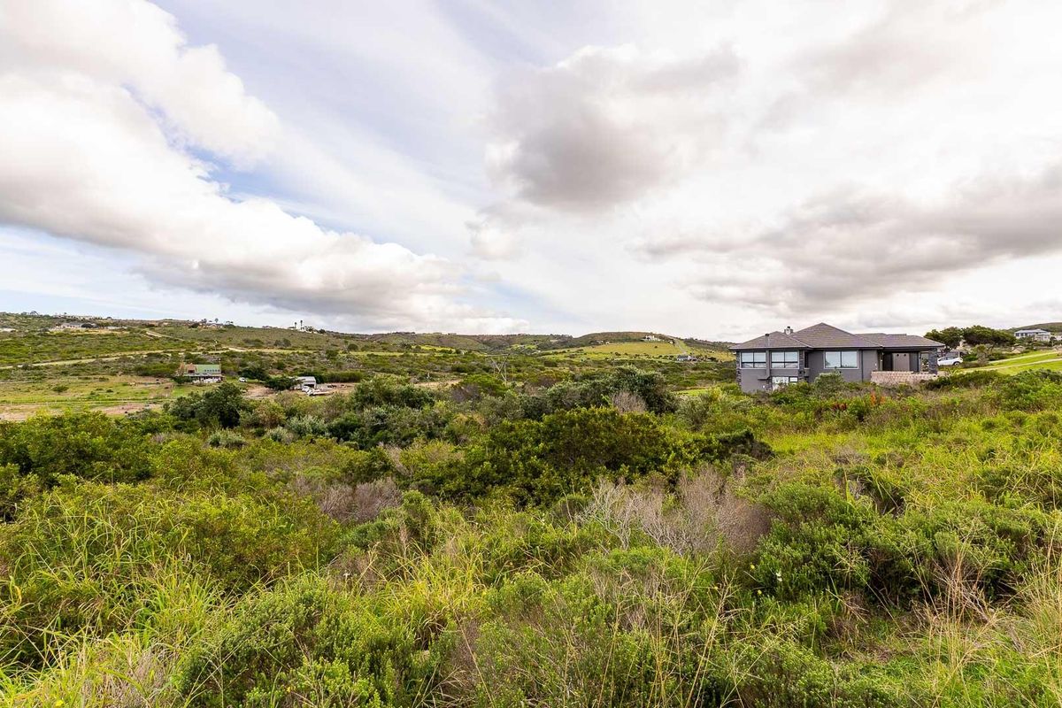 A wide-angle view of the vacant residential land featuring natural coastal vegetation and rolling terrain with neighboring properties visible in the distance.