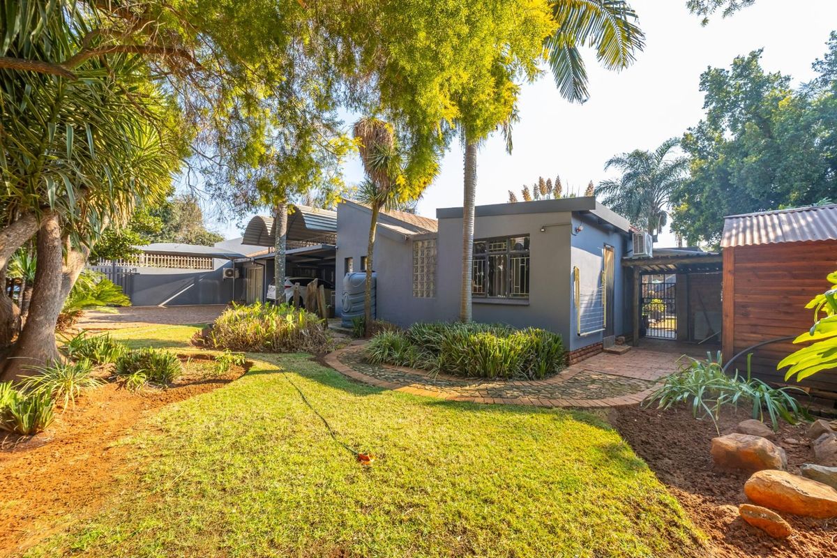 Rear view of the property featuring a landscaped garden, paved pathways, a carport, and a secure outdoor area with established trees.