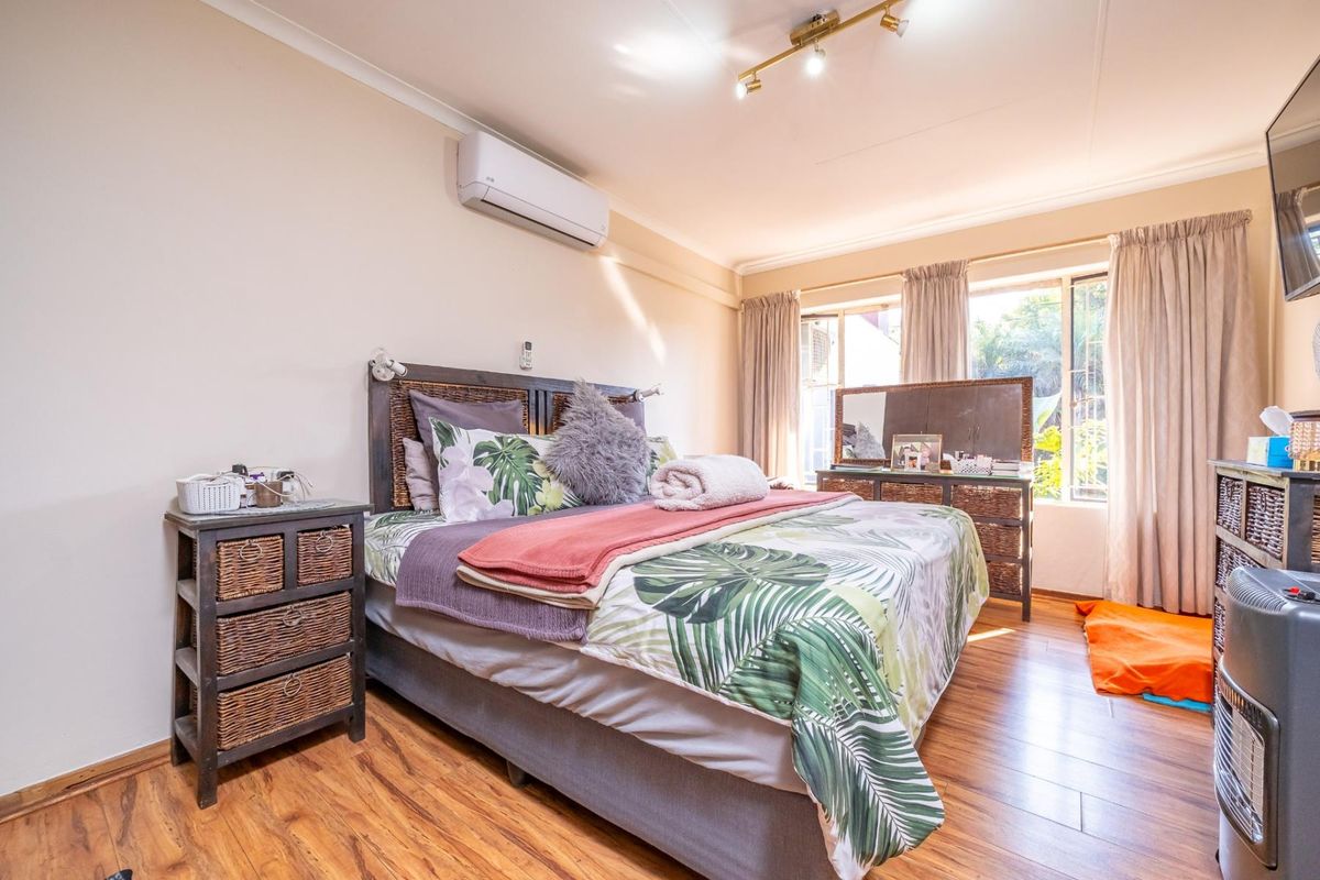 A well-maintained bedroom featuring laminate flooring, a wall-mounted split-system air conditioner, and track lighting, offering a comfortable and functional living space.