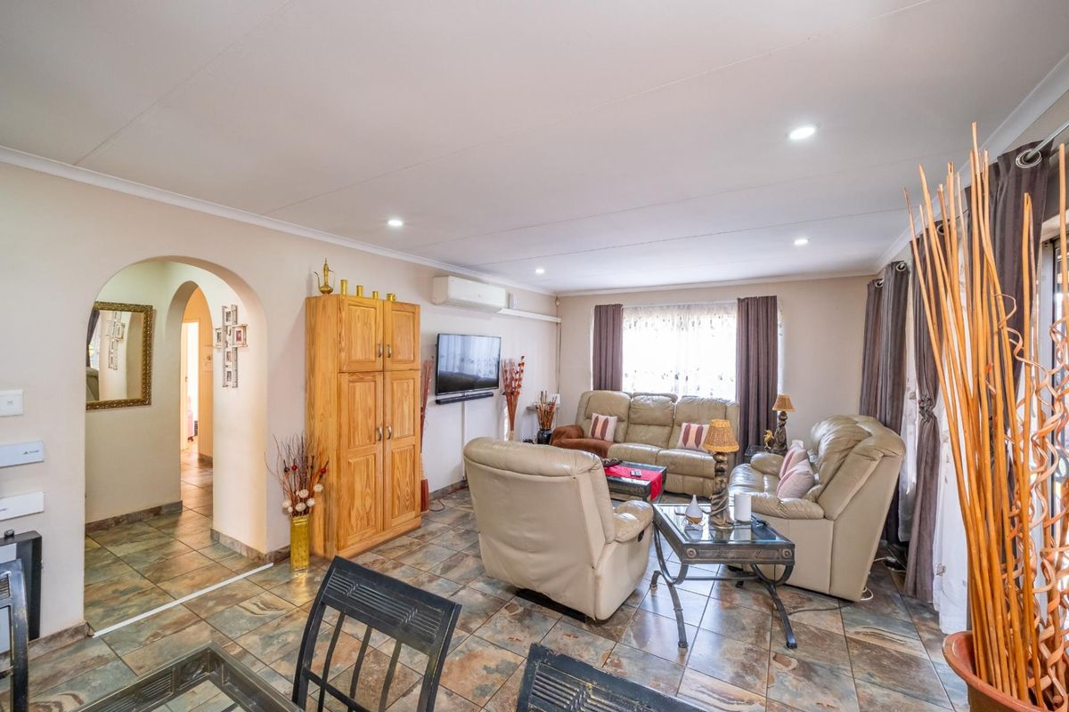 A spacious living room featuring tiled flooring, recessed downlighting, and a distinctive arched entryway leading to the hallway.
