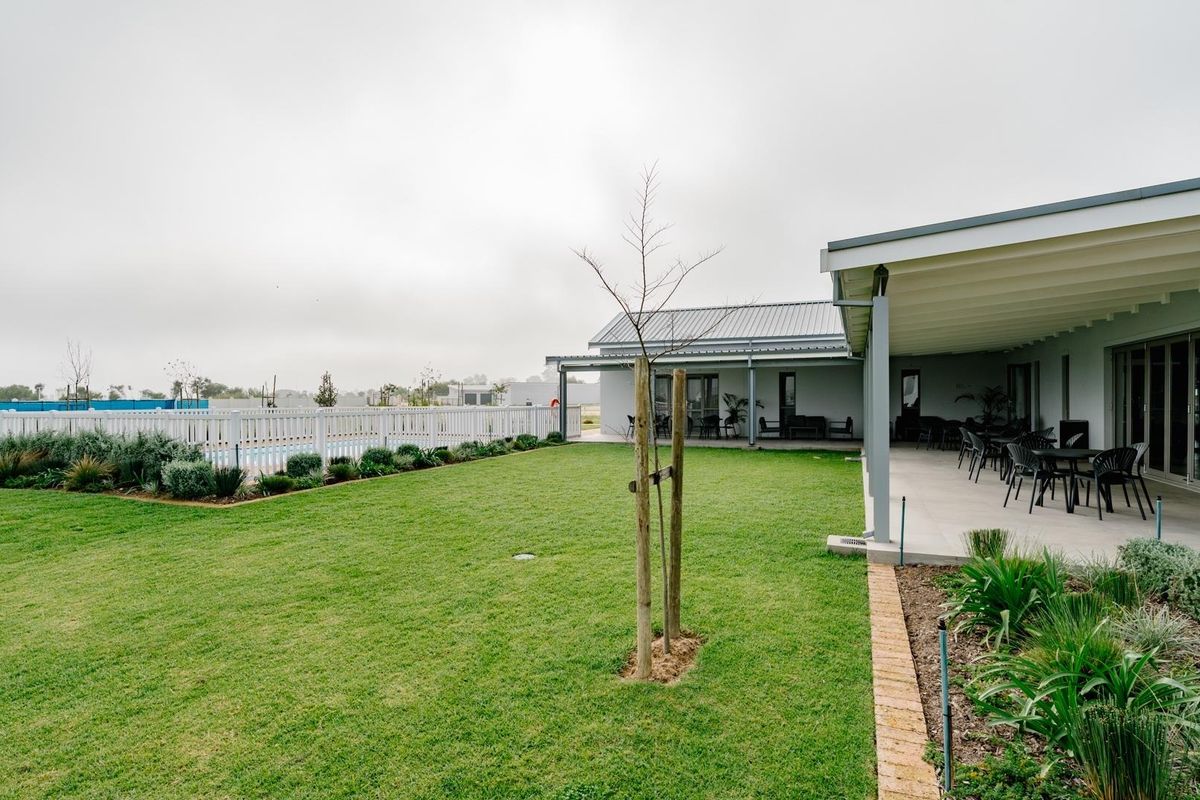 A spacious rear garden featuring a well-maintained lawn, a covered patio area, and a fenced swimming pool, ideal for outdoor entertaining.