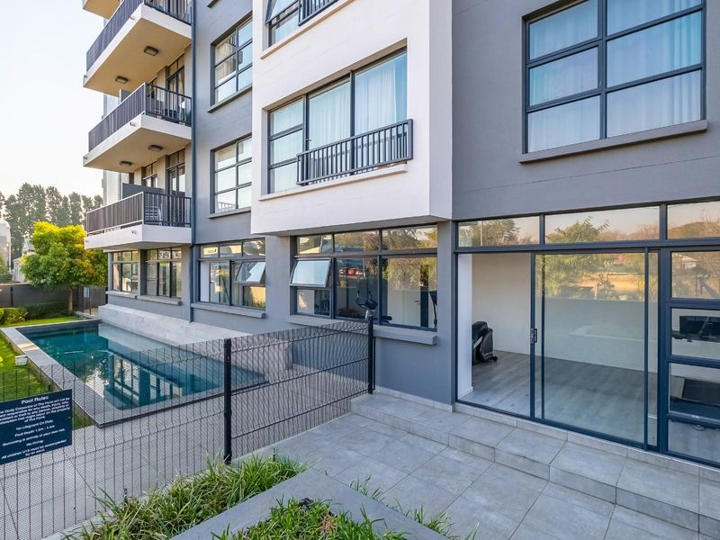 Exterior view of a modern apartment building featuring a swimming pool, ground floor patio access, and multiple levels of private balconies.