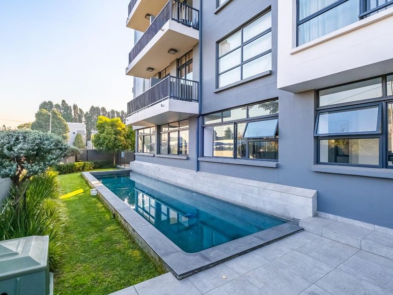 A modern apartment complex featuring a sleek lap pool, landscaped garden, and private balconies with contemporary aluminium window frames.