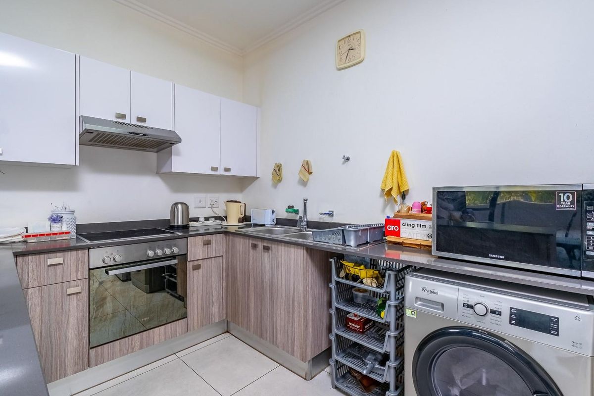 A functional kitchen featuring modern laminate cabinetry, a built-in oven with hob, extractor fan, stainless steel sink, and an integrated washing machine.