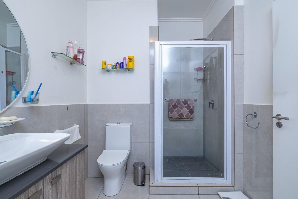 A modern bathroom featuring a vanity with a vessel sink, a toilet, and a glass-enclosed shower with neutral wall and floor tiling.