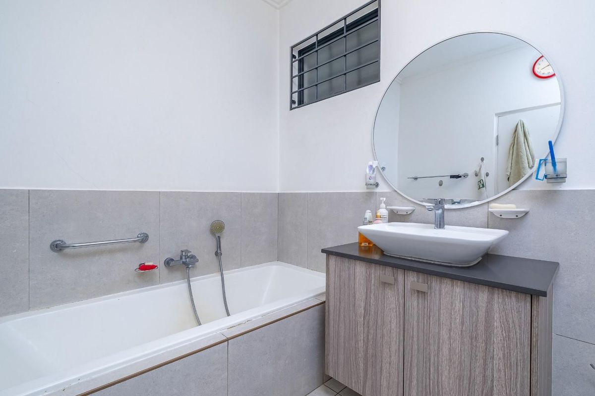 A clean, functional bathroom featuring a built-in bathtub with a handheld shower, a modern vessel sink on a vanity cabinet, and a large round mirror.