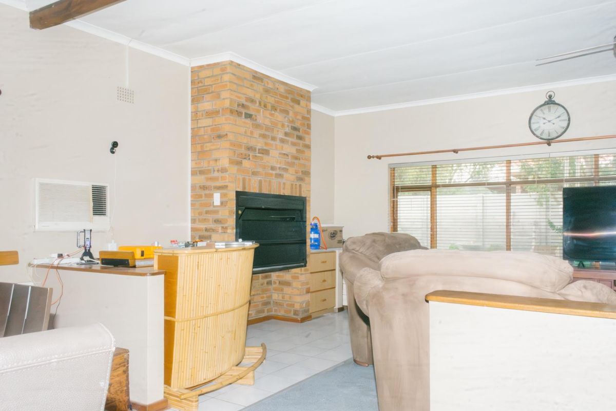 Living room featuring a prominent brick fireplace, tiled flooring, and a wall-mounted air conditioning unit, offering a functional space with potential for modernization.