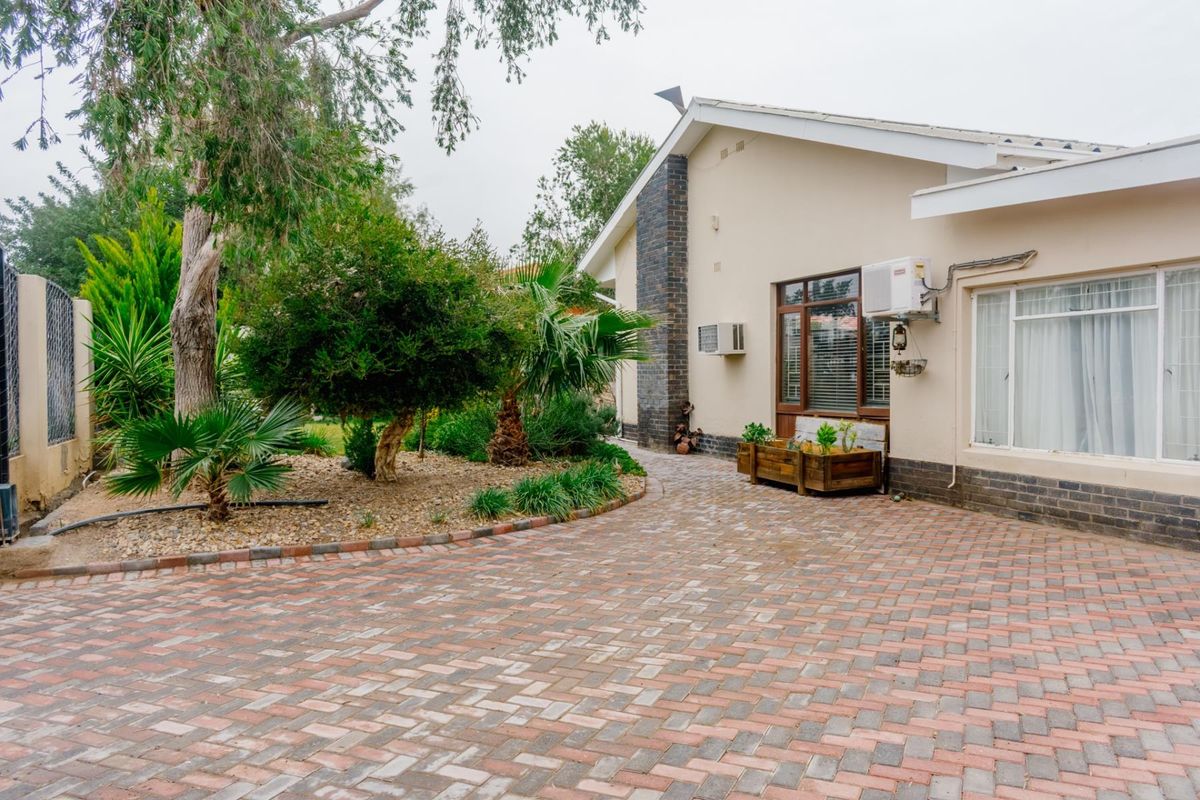 A well-maintained rear exterior view featuring a brick-paved courtyard, established garden landscaping, and a clean building facade with integrated air conditioning units.
