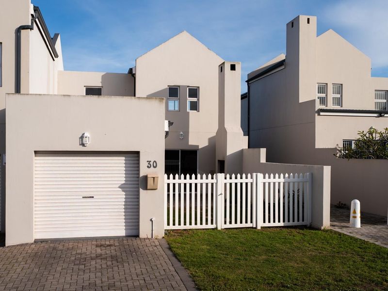 Front elevation of a townhouse featuring a single garage, paved driveway, white picket fence, and a chimney stack.
