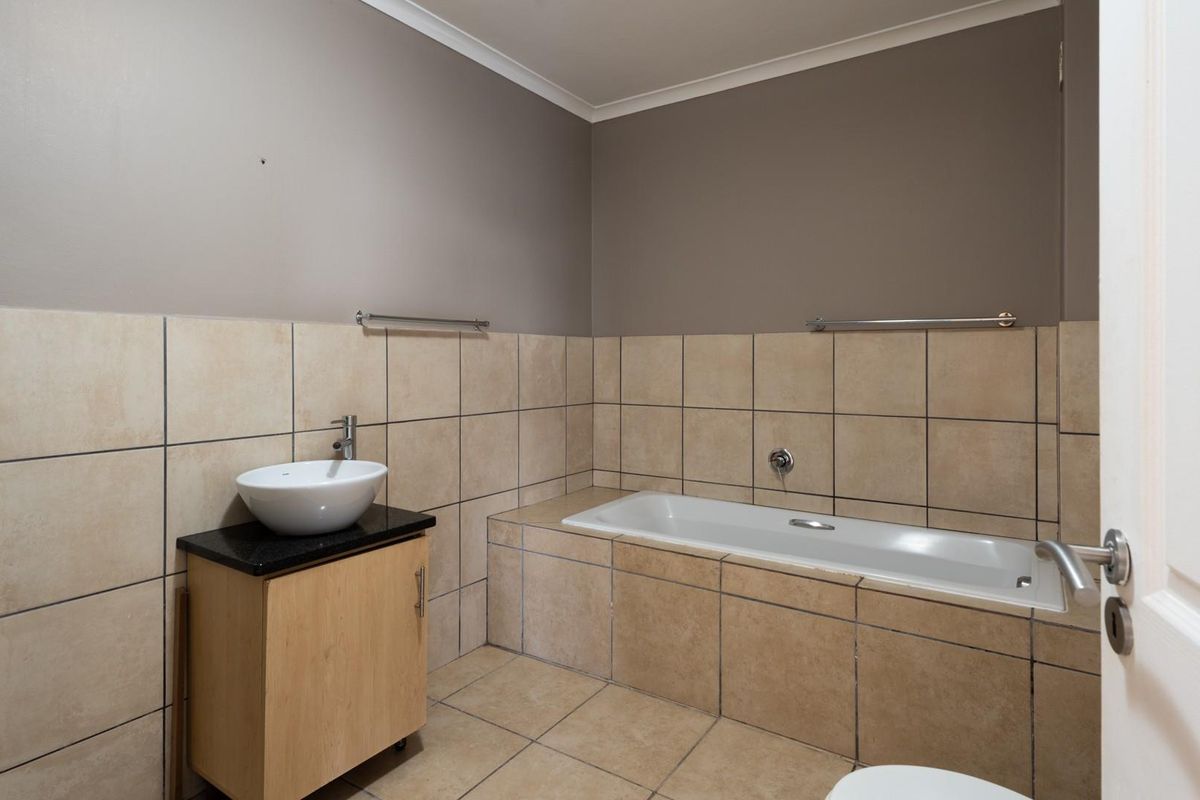 A functional bathroom featuring a built-in bathtub, a vanity cabinet with a vessel sink, and neutral-toned wall and floor tiling.