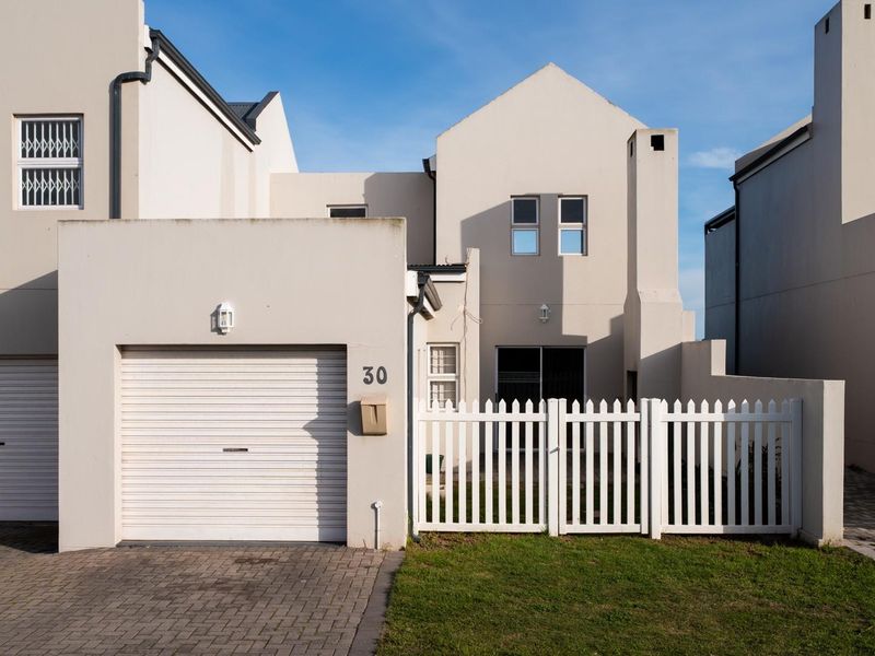 Front elevation of a modern townhouse featuring a single garage, paved driveway, and a white picket fence enclosing a small front garden area.