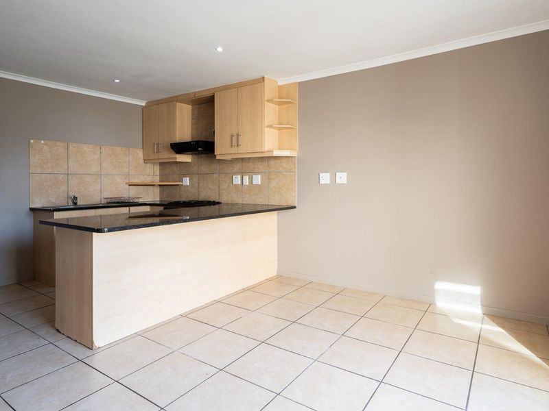 An open-plan kitchen area featuring light wood cabinetry, granite countertops, and neutral ceramic floor tiles in a clean, vacant space.