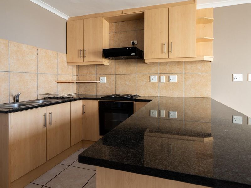 A functional kitchen featuring light wood cabinetry, dark granite countertops, a built-in oven, gas hob, and a tiled backsplash.