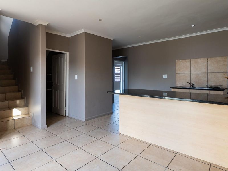 An open-plan living and kitchen area featuring tiled floors, granite countertops, built-in cabinetry, and a staircase leading to the upper level.