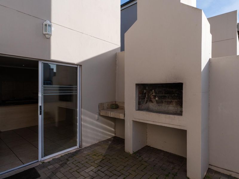 A private paved patio area featuring a built-in braai and direct access to the interior through a sliding glass door.