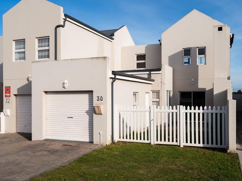 Front elevation of a townhouse featuring a single garage, paved driveway, and white picket fencing with security bars on windows.