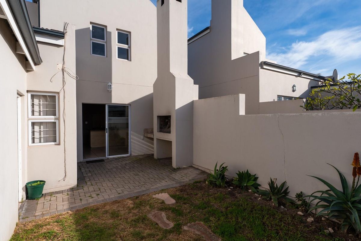 Rear townhouse courtyard featuring a paved patio area, built-in braai, and a small garden space with boundary walling.