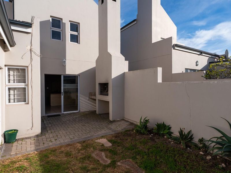 Rear townhouse courtyard featuring a paved patio area, built-in braai, and a small garden space with boundary walling.