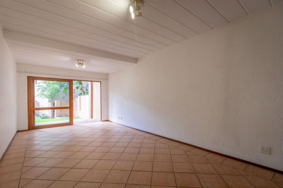 A spacious, empty living room featuring tiled floors, textured walls, exposed beam ceilings, and a large sliding glass door providing access to the exterior.