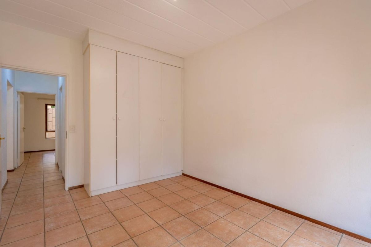 An empty bedroom featuring built-in cupboards, tiled flooring, and a panelled ceiling, with a view into the adjacent hallway.