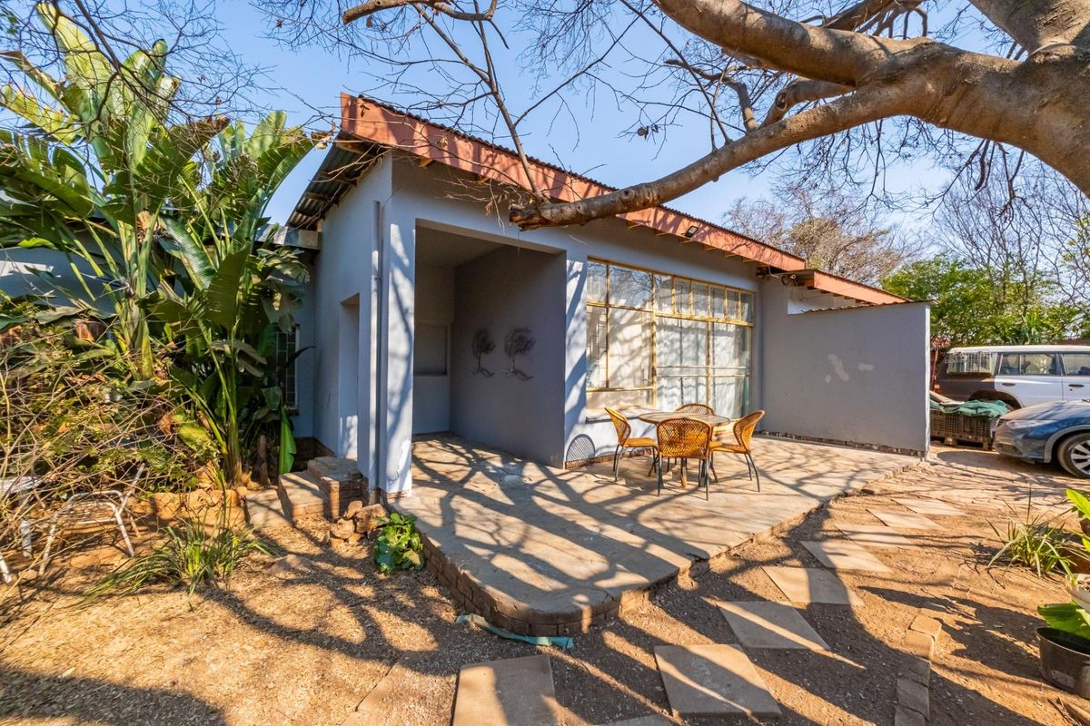 Rear exterior view of the house featuring a covered patio area, steel-framed windows, and a paved walkway leading through the garden.