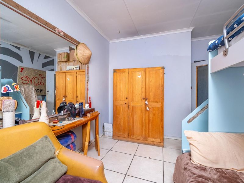 A bedroom featuring tiled flooring, a built-in wooden wardrobe, and coved ceilings, currently requiring cosmetic updates to the wall finishes.